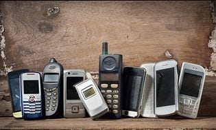 Gamle mobiltelefoner på en lang række foran træværk