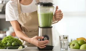 En kvinde blender en grøn smoothie ved et køkkenbord