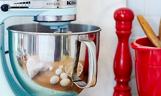 Blå KitchenAid foran æggeskaller og rødt køkkengrej i et køkken
