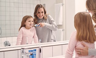 Kvinde hjælper sit barn med at børste sine tænder med en Oral-B elektrisk tandbørste