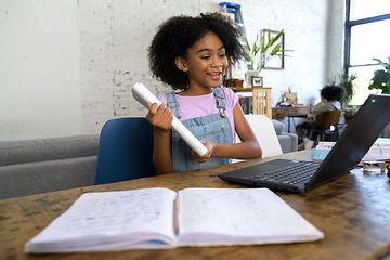 Lille pige laver lektier med en bærbar og en bog foran hende
