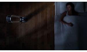 Kvinde, der ligger i sengen og sover ved siden af en Dyson Cool tårnvifte i et mørkt soveværelse