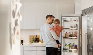Mand holder et barn i et hvidt køkken