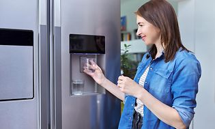 En kvinder står ved et køleskab og fylder vand i et glas 