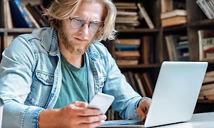Mand arbejder på laptop og ser på sin telefon