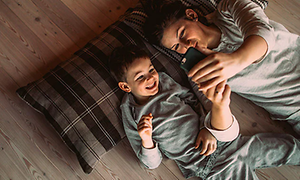 En kvinde og et barn ligger på gulvet og ser på en smartphone
