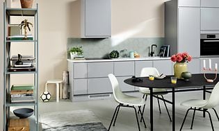 Lysegråt EPOQ Integra køkken i en åben køkkenløsning med spisebord, stole og en bogreol