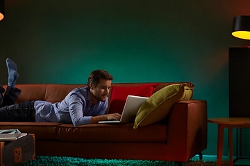 Man ligger på sofa og bruger en bærbar med forskellige lamper i nærheden