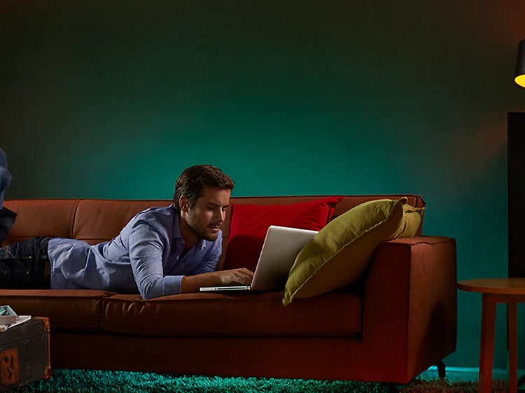 Man ligger på sofa og bruger en bærbar med forskellige lamper i nærheden