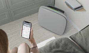 En grå Well 5 på gulvet og en person med Wellbeing-appen på sin telefon