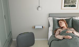 En kvinde sover i sin seng med en grå Well A7 ved siden af hende på gulvet