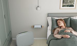En dame, der sover i sin seng med en grå Well 5 på gulvet ved siden af sig