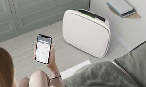 En hvid Well A5 på gulvet og en person med Wellbeing-appen på sin telefon