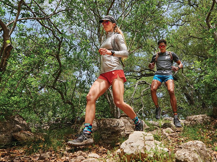 Garmin Fenix 7 på armene på en kvinde og en mand, der løber i vildmarken