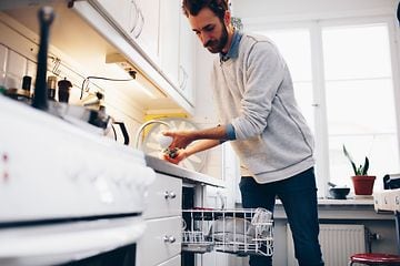 En mand, der vasker en kaffekop, stående foran en åben opvaskemaskine