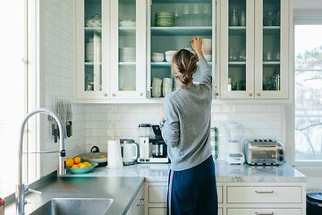 Kvinde sætter ting på plads i sine køkkenskabe