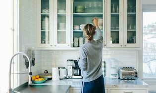 Kvinde sætter ting på plads i sine køkkenskabe