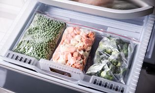 Tre plastikposer med frosne grøntsager i en fryser