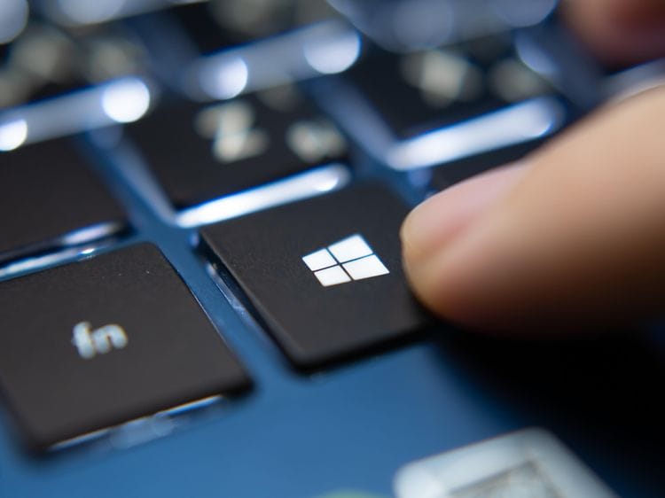 Finger der trykker på Microsoft Windows knappen på en blå laptop