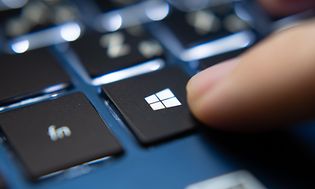 Finger der trykker på Microsoft Windows knappen på en blå laptop