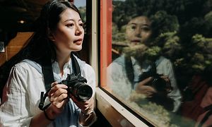 Kvinde sidder med DSLR kamera i hånden i et tog