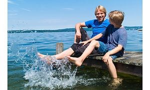 To drenge plasker med benene i vandet fra en bro