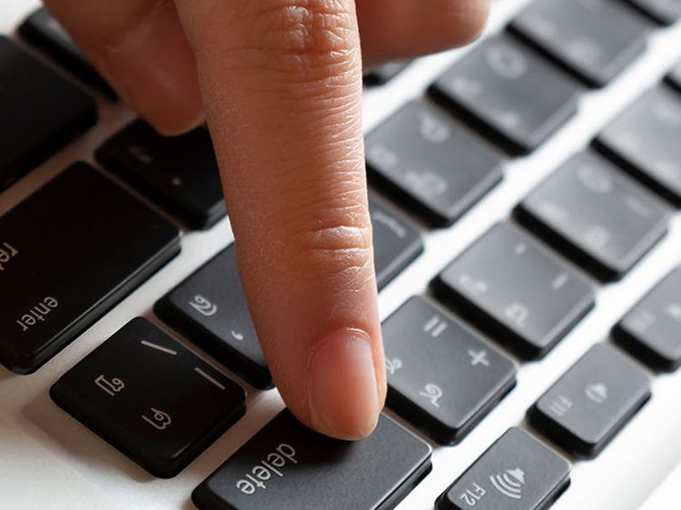 En hånd, der trykker på sletteknappen på en bærbar computer