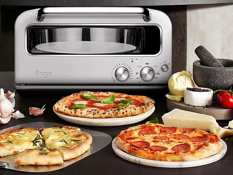 Forskellige typer pizza på bord og en Sage pizzaovn i baggrunden