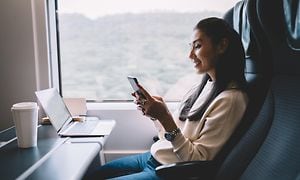 Kvinde bruger telefonen i et tog med sin pc på bordet foran hende