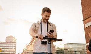 Wearables - Mandlig turist står stille med en el-scooter og tjekker sin telefon