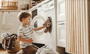 Dreng lægger en bamse ind i en vaskemaskine