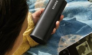 Sonos Roam i hånden på kvinde ved siden af smartphone