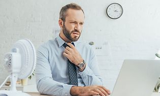 Mand har det for varmt på kontoret og køler sig ned med en blæser