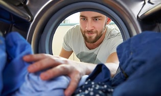 Mand der tager sit vasketøj ud af maskinen