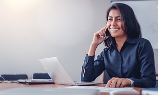 En kvinde, der arbejder på sin bærbare computer og taler på sin smartphone