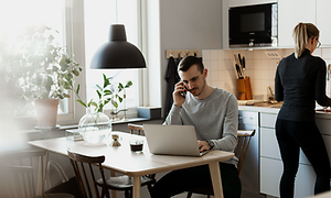 En mand, der arbejder på sin bærbare computer og taler på sin smartphone i et køkken