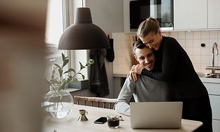 Par i et køkken foran en bærbar computer