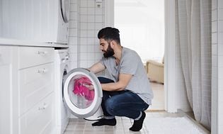 Mand fylder tøj i en vaskemaskine