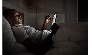 Mand, der ligger i sengen og arbejder med en digital pen på en skærm.