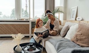 To kvinder i en sofa læser en bog og har en luftrenser bag dem