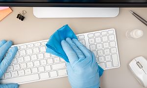 Hånd med blå gummihandske rengører et tastatur