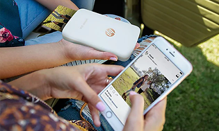 Folk, der holder HP Sprocket-printer og smartphone med en åben app