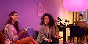 2 kvinder sidder i en sofa. Den ene betjener smartlyset med fjernbetjening.