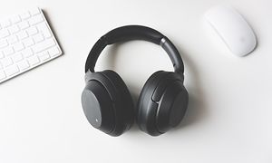 Sorte høretelefoner på et hvidt bord med hvid mus og tastatur