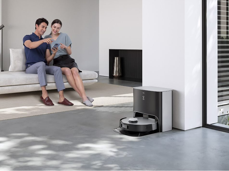 En Ecovacs Deebot X1 Plus oplader mens en mand og kvinde sidder i baggrunden