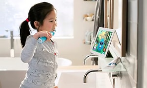 En pige, der børster tænder med en elektrisk tandbørste, mens hun ser tablet