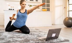 Kvinde dyrker yoga, mens hun arbejder derhjemme