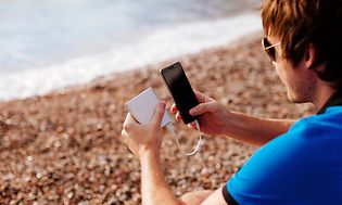 Mand på strand oplader sin smartphone med en powerbank