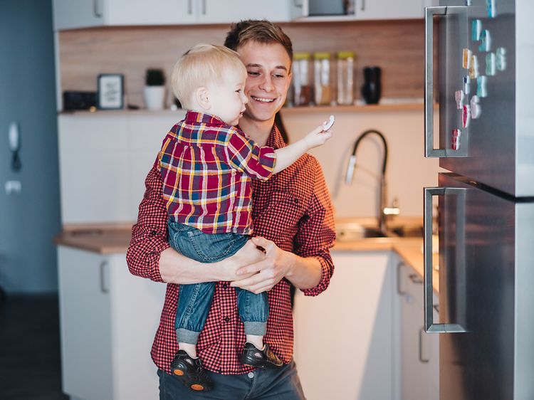 Mand holder en lille dreng foran en køleskab i børstet stål