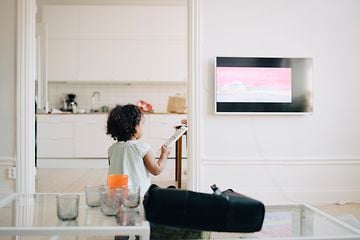 Lille pige med fjernbetjening i hånden foran TV